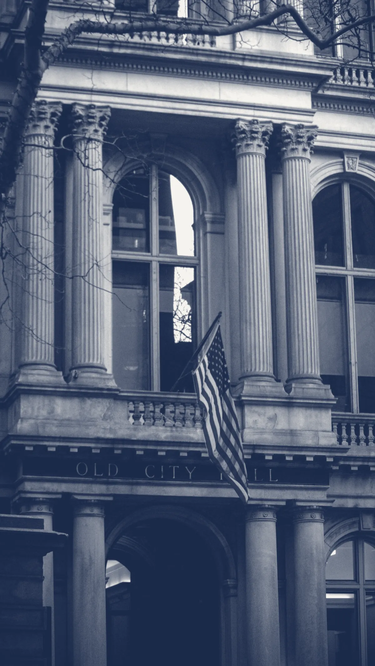 An American flag on a historic city hall, in JAG's navy-and-paper duotone.