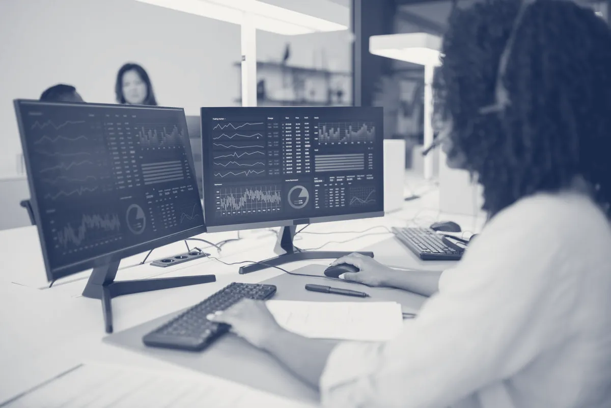 An analyst working across data screens, in JAG's navy-and-paper duotone.